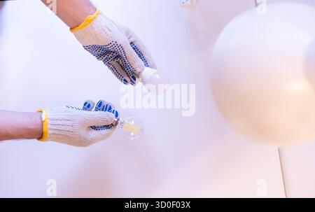Hands in protective gloves holding two different light bulbs:energy-saving LED and filament type. Concept of choosing the right lamp for home lighting Stock Photo