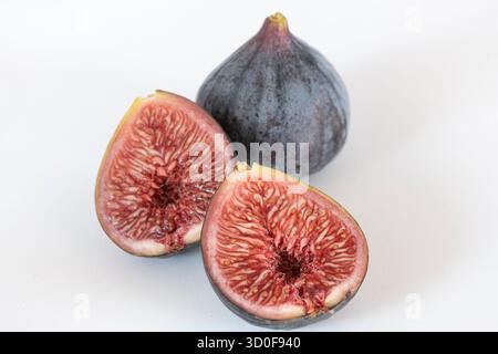 Whole and halved Black Mission figs displayed on a clean white background, showcasing the fruits deep purple skin, soft texture Stock Photo