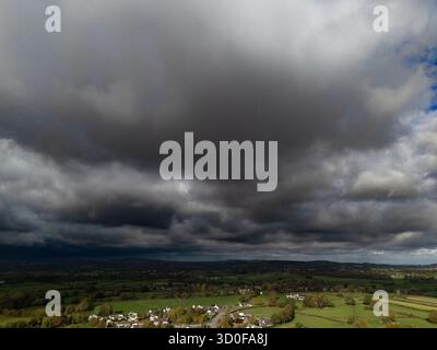 An aerial view shows a storm rolling in over a rural landscape, with dark, ominous clouds dominating the sky above fields and a small village. Stock Photo