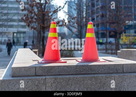 Two bright orange traffic cones with yellow stripes placed on a stone surface in an urban setting in Seoul, South Korea on 20 March 2024 Stock Photo