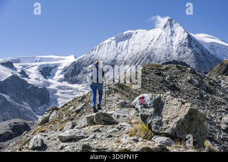 Female hiker hiking on a rocky path towards snow-covered mountain peaks under clear skies, Mont Blanc de Cheilon mountain summit with glacier, Herme Stock Photo