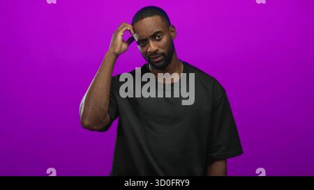 Man scratching head and touching temple with right hand in purple studio, wearing black t shirt and gold chain; confusion doubt puzzlement. Stock Photo