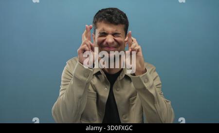 Man holds fingers crossing background while male hispanic young colored backdrop guy hopes. Stock Photo