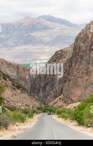View of a long road stretching between towering cliffs under a vast sky, leading toward distant mountains, a serene journey, Magellan Cave, Vayots Dzor Province, Armenia. Stock Photo