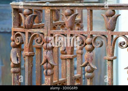 Close-up of an old, ornate, rusty iron fence with floral accents. Stock Photo