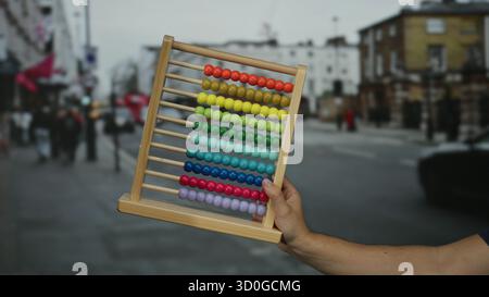 Man holding colorful abacus on a busy city street showcasing urban education and creativity amidst a bustling outdoor environment. Stock Photo