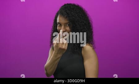Young smiling friendly woman standing confidently beckons with finger against pink studio wall; invitation. Stock Photo