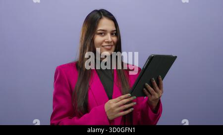 Young woman in a vibrant pink jacket using a digital tablet against a purple background, embodying modern technology and youthful energy. Stock Photo