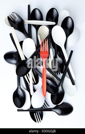 A red plastic fork on top of a pile of black and white plastic spoons and forks Stock Photo