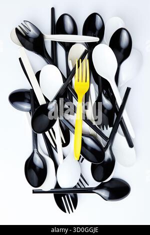 A yellow plastic fork on top of a stack of black and white cutlery Stock Photo
