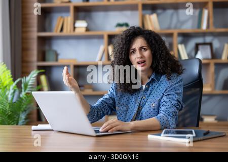 Confused young woman engaging in remote work, experiencing technical difficulties and looking frustrated while sitting at desk with laptop in coworking space Stock Photo
