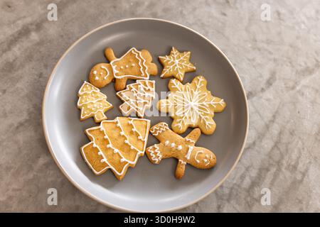 Round grey plate holding iced gingerbread people, tree and snowflake cookies on marble countertop Stock Photo
