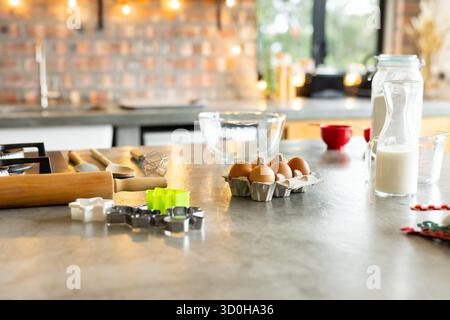 Home kitchen counter displaying eggs, mixing bowl, milk bottle near brick wall with lights Stock Photo