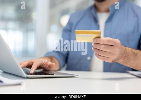 Man holding a credit card while typing on a laptop, performing a secure online transaction or shopping, illustrating digital banking and e-commerce concepts Stock Photo