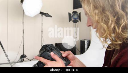 Examining man adjusting DSLR settings in studio, with backdrop and softbox spotlight, copy space Stock Photo