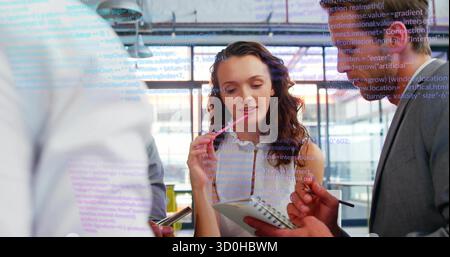 Reviewing code projected on glass by team in office in business attire with notebook and smartphone Stock Photo