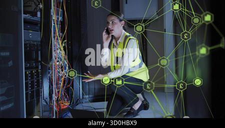 Kneeling tech wearing safety vest checking cables in data center, neon green overlay and smartphone Stock Photo