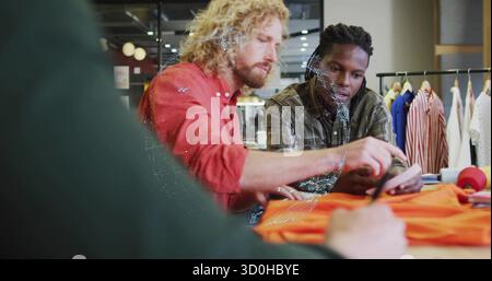 Examining shoe, two designers collaborating at fashion studio table, with fabric rolls and scissors Stock Photo