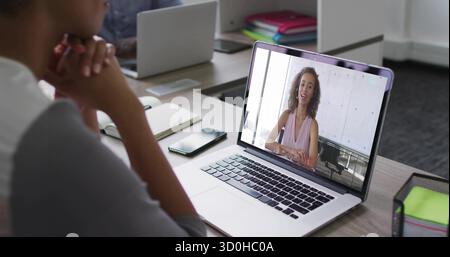 Displaying silver laptop showing woman speaking in virtual call at office, with wire mesh organizer Stock Photo