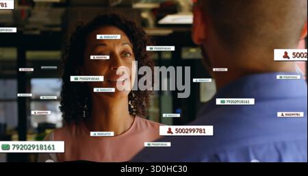 Curly-haired woman in pink blouse addressing man at office with floating data tags, copy space Stock Photo