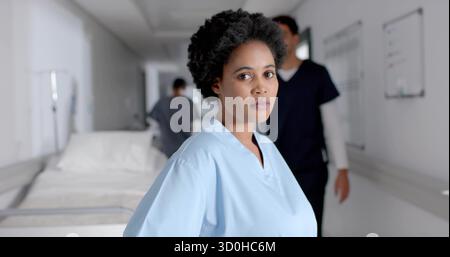 Standing nurse wearing light blue scrubs in hospital corridor, with gurney and whiteboard Stock Photo