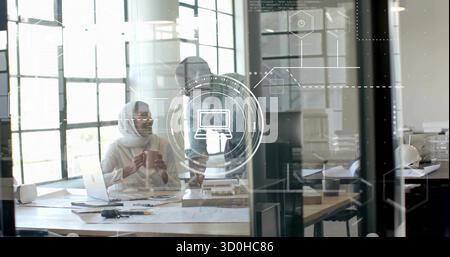 Collaborating professionals examining scale model and blueprints in office, with laptop and mug Stock Photo
