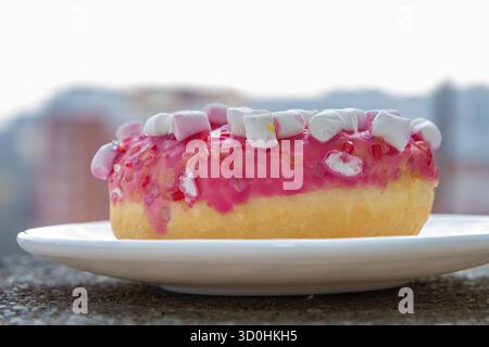 Pink donut with marshmallows on white plate Stock Photo