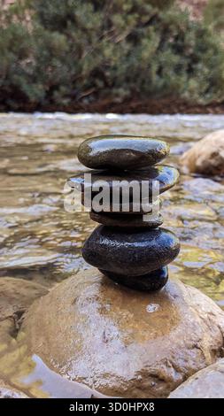 stack of smooth, wet stones balanced on a rock in a flowing river - symbolizing balance, mindfulness, and harmony with nature Stock Photo