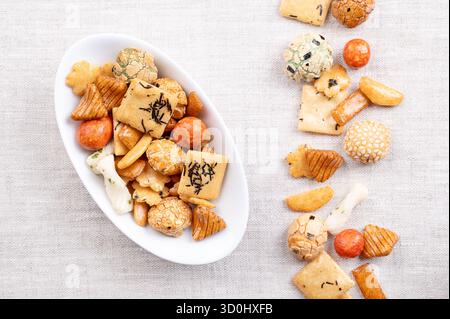 Japanese rice crackers, in white bowl, on linen. Assorted varieties of Arare crackers made from baked rice flour, brushed with soy sauce and vinegar. Stock Photo