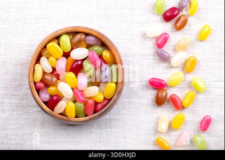 Jelly beans, flavor and color assortment, in a wooden bowl, on linen. Small bean-shaped sugar candies with soft candy shells and thick gel interiors. Stock Photo