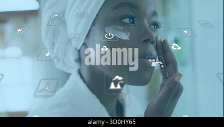Applying woman wearing robe and towel smoothing eye cream at bathroom mirror, AR icons, copy space Stock Photo