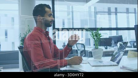 Interacting red-shirted Middle Eastern man selecting on laptop UI using stylus at office, by plant Stock Photo