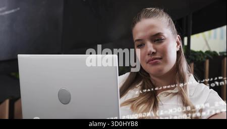 Typing woman wearing collared shirt coding in office, with laptop showing code overlay and planters Stock Photo