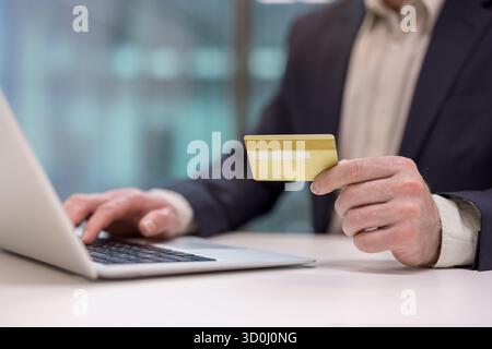 Man holding a gold credit card and typing on a laptop keyboard, making an online purchase or accessing internet banking in an e-commerce or digital finance concept Stock Photo