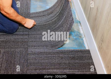 Worker carefully lays down gray carpet tiles in an office on precise alignment installation techniques. Stock Photo