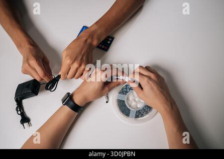 Closeup cropped shot of two technicians connecting RGB led strip lights, configuring wireless controller for personalized ambient lighting in dark Stock Photo