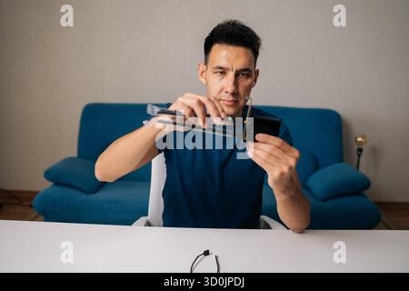 Technician male assembling wi-fi module by connecting antennas sitting at white table in home office, focused on ensuring optimal performance Stock Photo