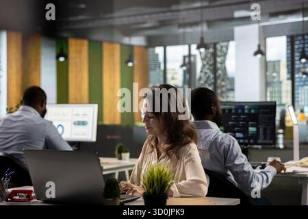 Business people gathered around laptops working on project tasks and targets for development. Office environment promotes synergy, teamwork and insight through analytics and planning. Stock Photo