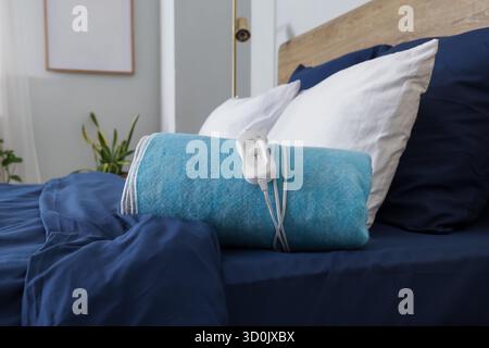 Folded electric heating pad on bed in room Stock Photo