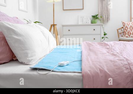Modern electric heating pad on bed in room Stock Photo