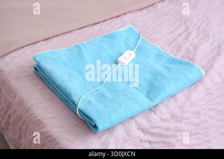 Modern electric heating pad on pink blanket in bedroom Stock Photo