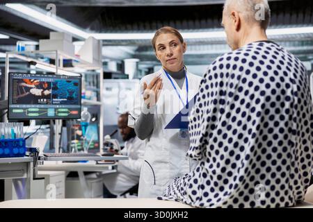 Woman pharmacology expert conduct tests on a senior man in modern research lab, observing side effects and chemical reactions. Scientist testing drug on patient to launch safe treatment. Stock Photo