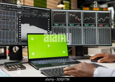 Close up of prop firm trader using green screen laptop on desk and computer displaying stock market candlestick graphs. Financial expert uses chroma key notebook and PC showing stock exchange assets Stock Photo