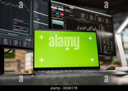 Close up of isolated screen laptop in brokerage office next to workstation monitor displaying live stock charts. Chroma key notebook device and PC with financial software in prop firm workspace Stock Photo