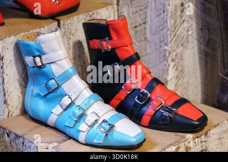 Close-up of John Fluevog ankle boots with multiple buckles in blue, white, red, and black leather on display. Stock Photo