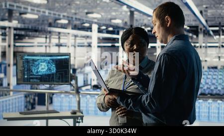 Team of engineers in server hub optimizing deep learning AI systems handling tasks. Teamworking data center colleagues adjust artificial intelligence model parameters using device, camera B Stock Photo