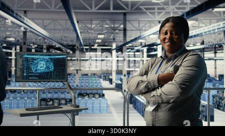 Portrait of smiling data center manager working to improve AI rigs processing speed and efficiency. Happy team leader in server hub manages gear to support artificial intelligence workloads, camera A Stock Photo