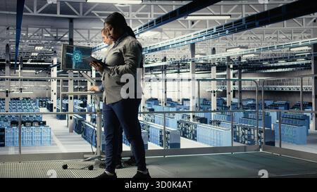 Data center software developers deploy machine learning software on infrastructure racks. Server room IT specialists train AI systems with datasets using tablet to support applications, camera A Stock Photo