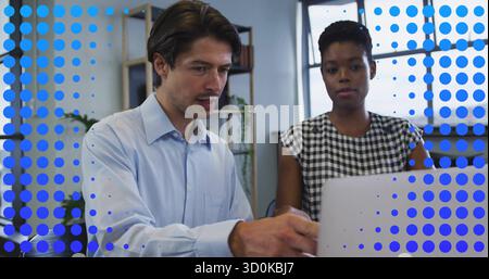 Two professionals in business attire collaborating over laptop in office with shelving and plants Stock Photo