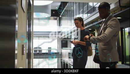 Standing pair wearing suits holding tote and using smartphones at elevator panel, with AR overlays Stock Photo